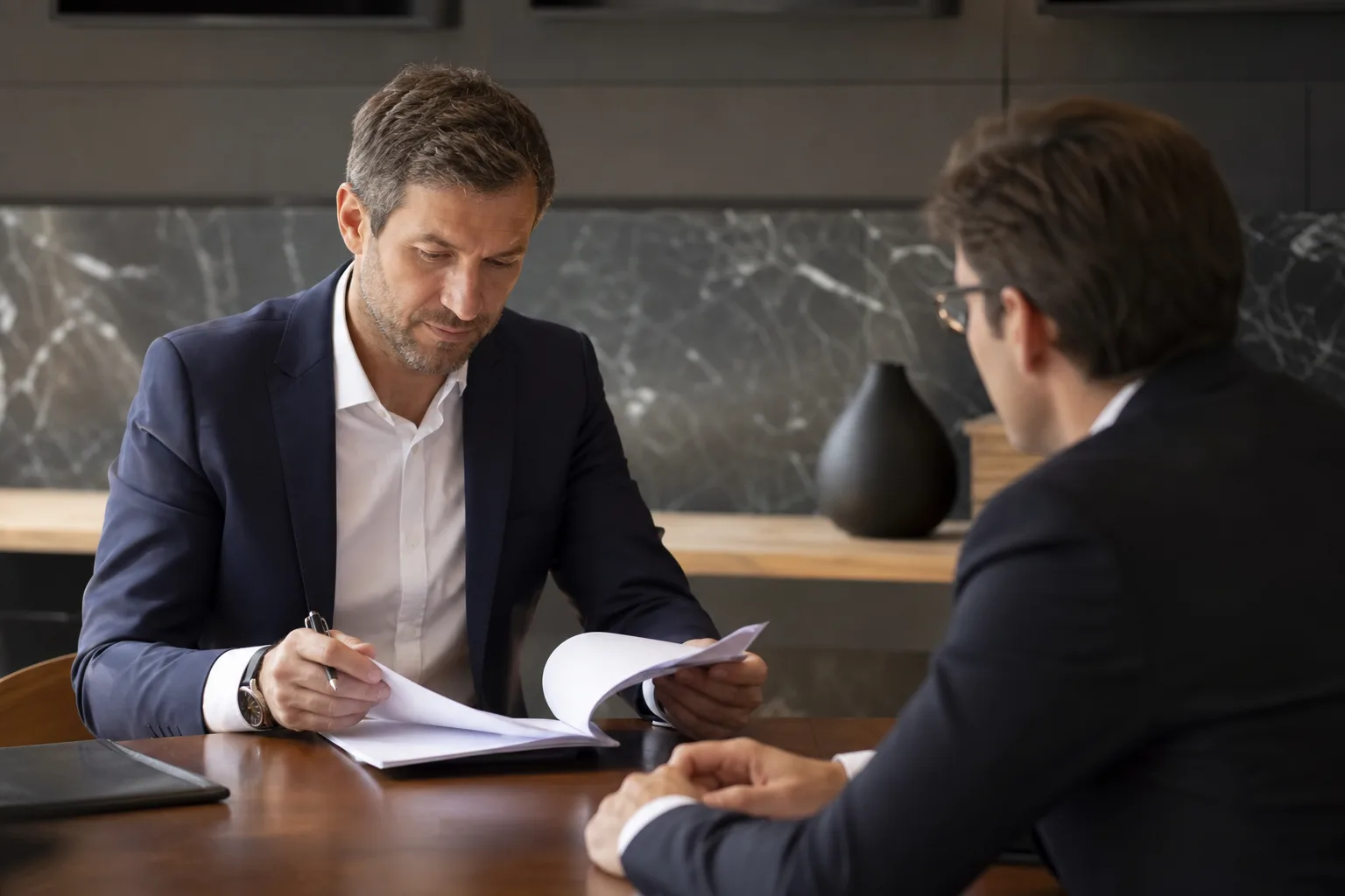 Dirigeant d'entreprise lisant attentivement un acte de cautionnement avec son conseiller, dans un bureau sobre et lumineux.