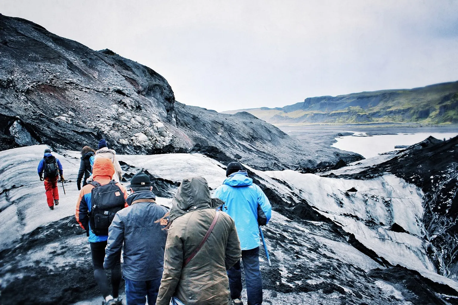 Une scientifique équipée sur un glacier relève des instruments de mesure face à un paysage alpin.