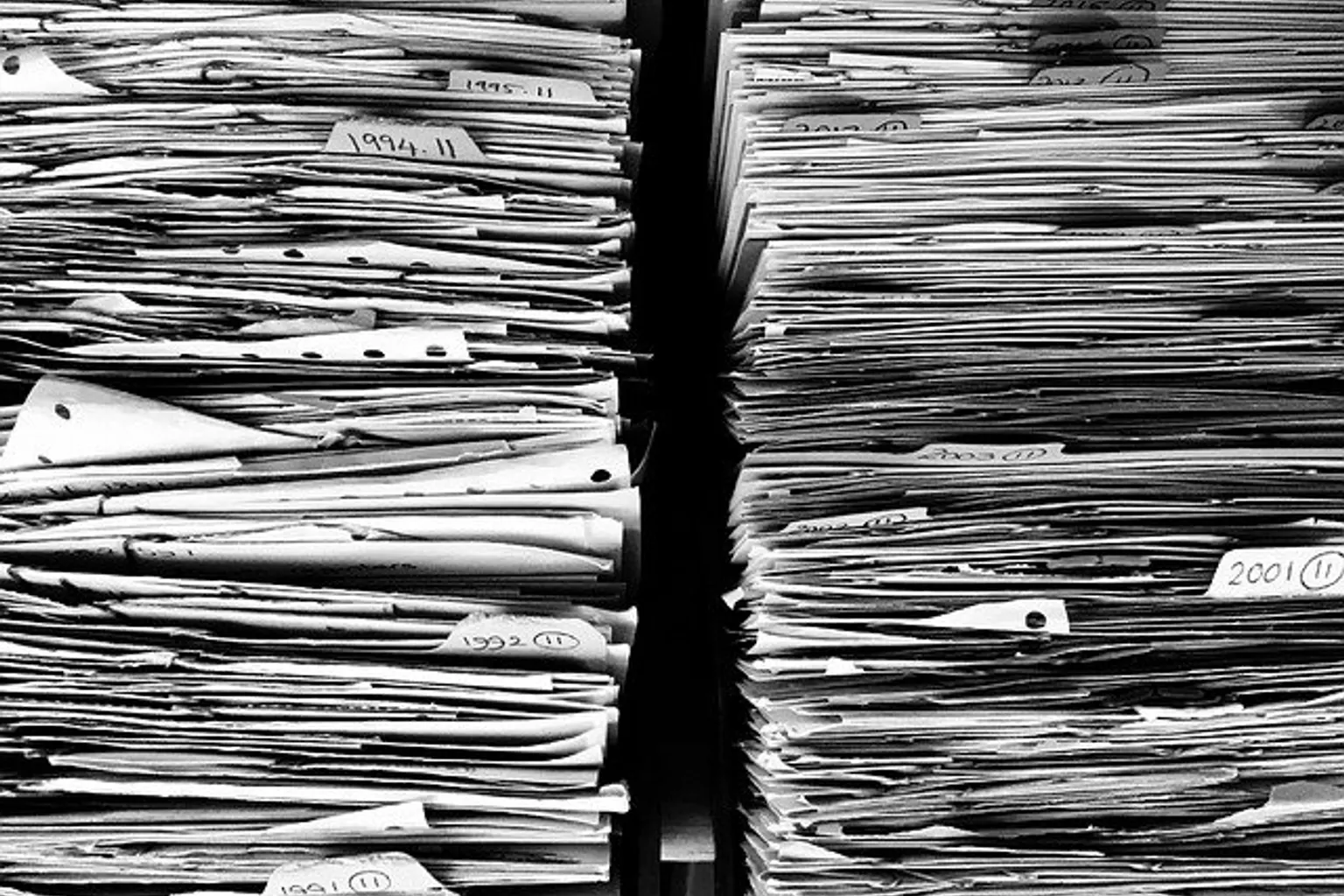 Dossiers d’entreprise étiquetés et archivés sur des étagères, à côté d’un ordinateur affichant une solution de gestion documentaire.